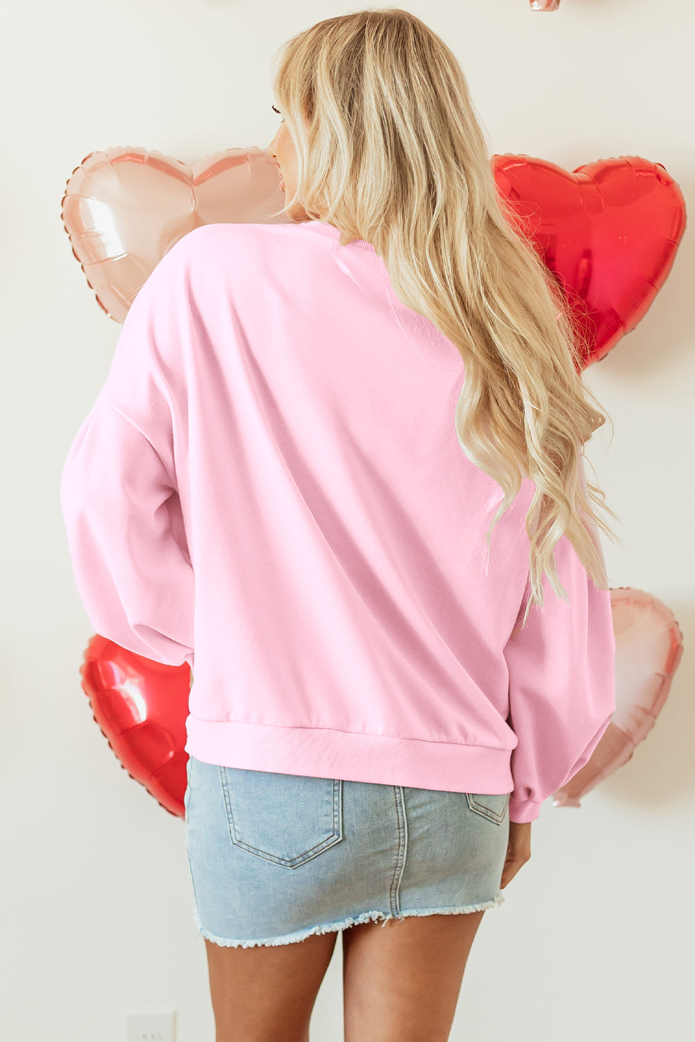 Person wearing a pink sweatshirt with heart-shaped balloons in the background