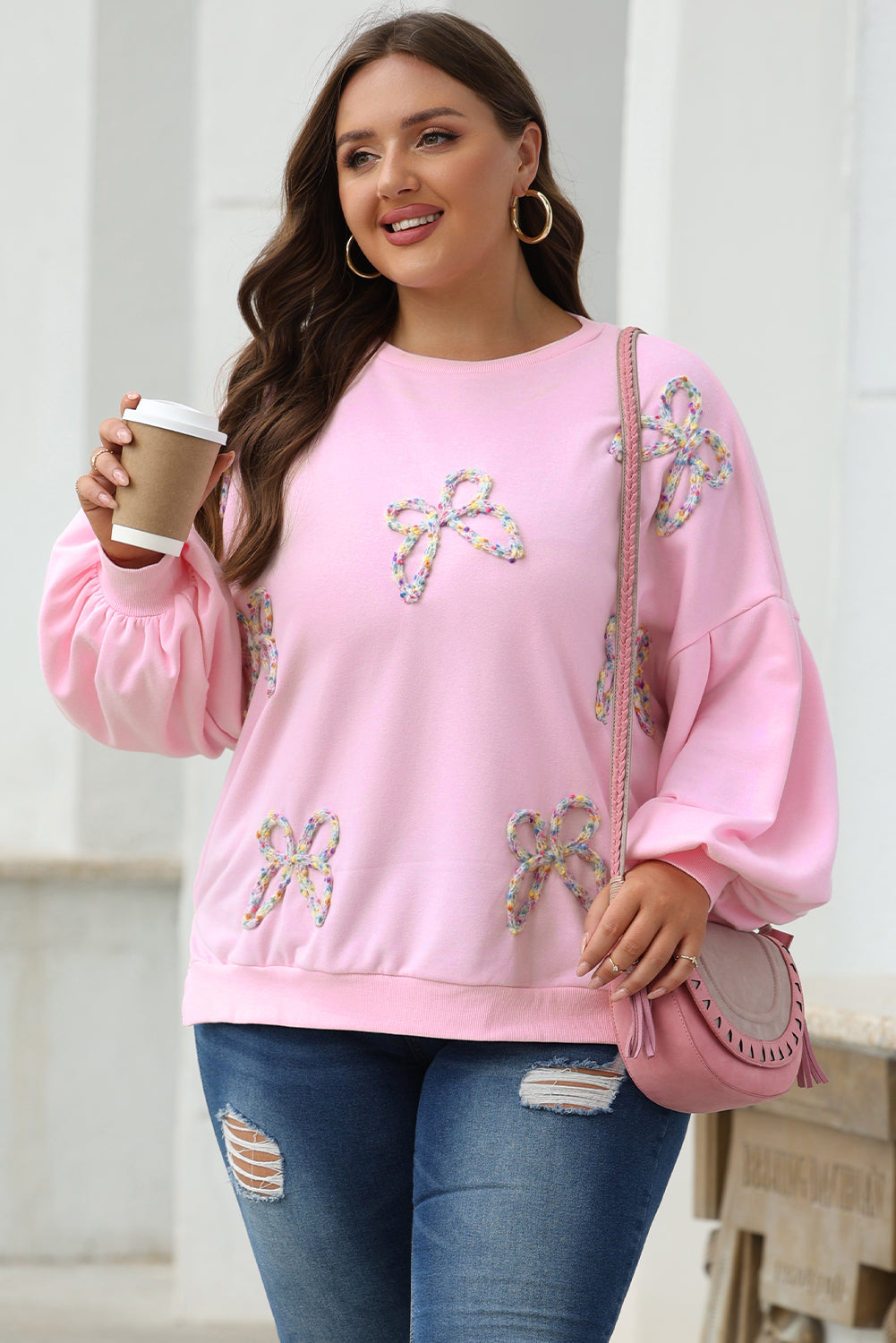 Woman wearing a pink sweater with floral embellishments, holding a coffee cup.