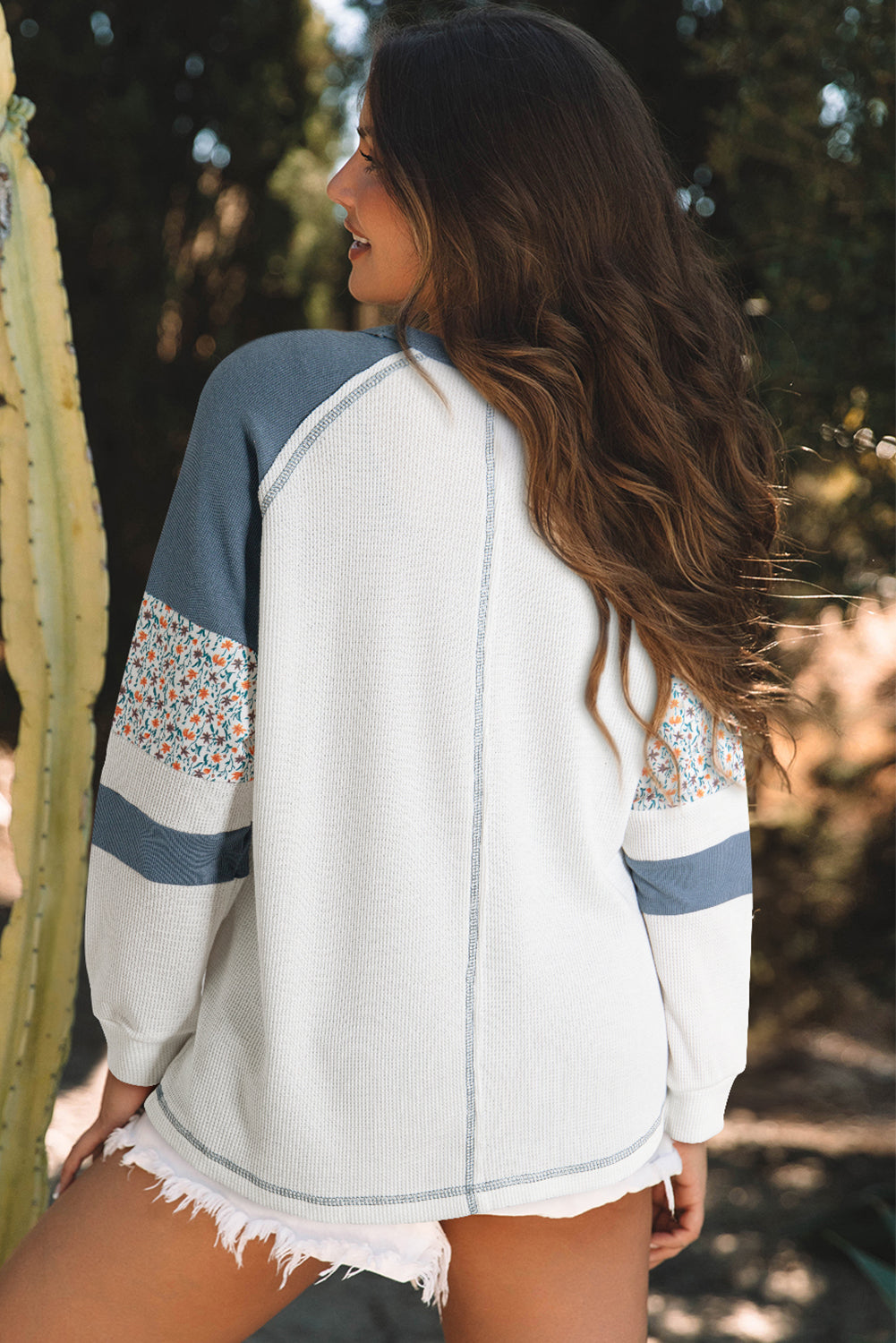 Woman wearing a white sweater with blue and floral sleeves, standing outdoors.