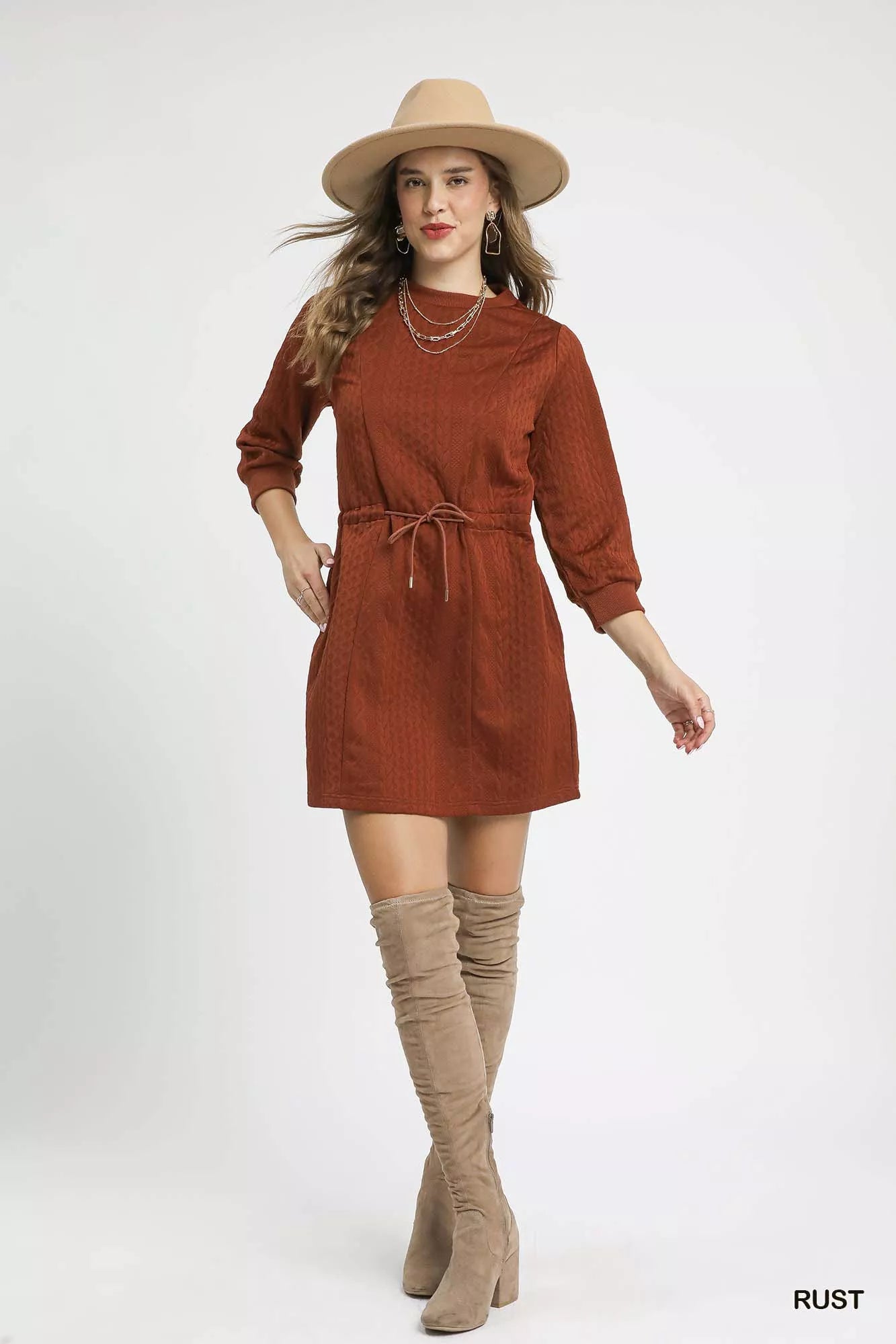 Woman wearing a rust-colored dress with a hat and knee-high boots on a white background