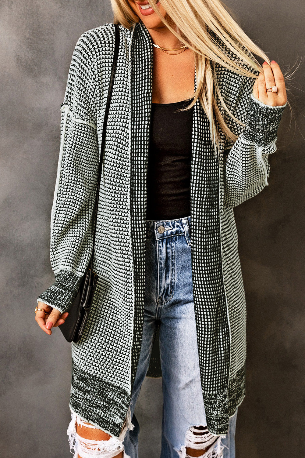 Person wearing a long, patterned cardigan over a black top and jeans against a gray background