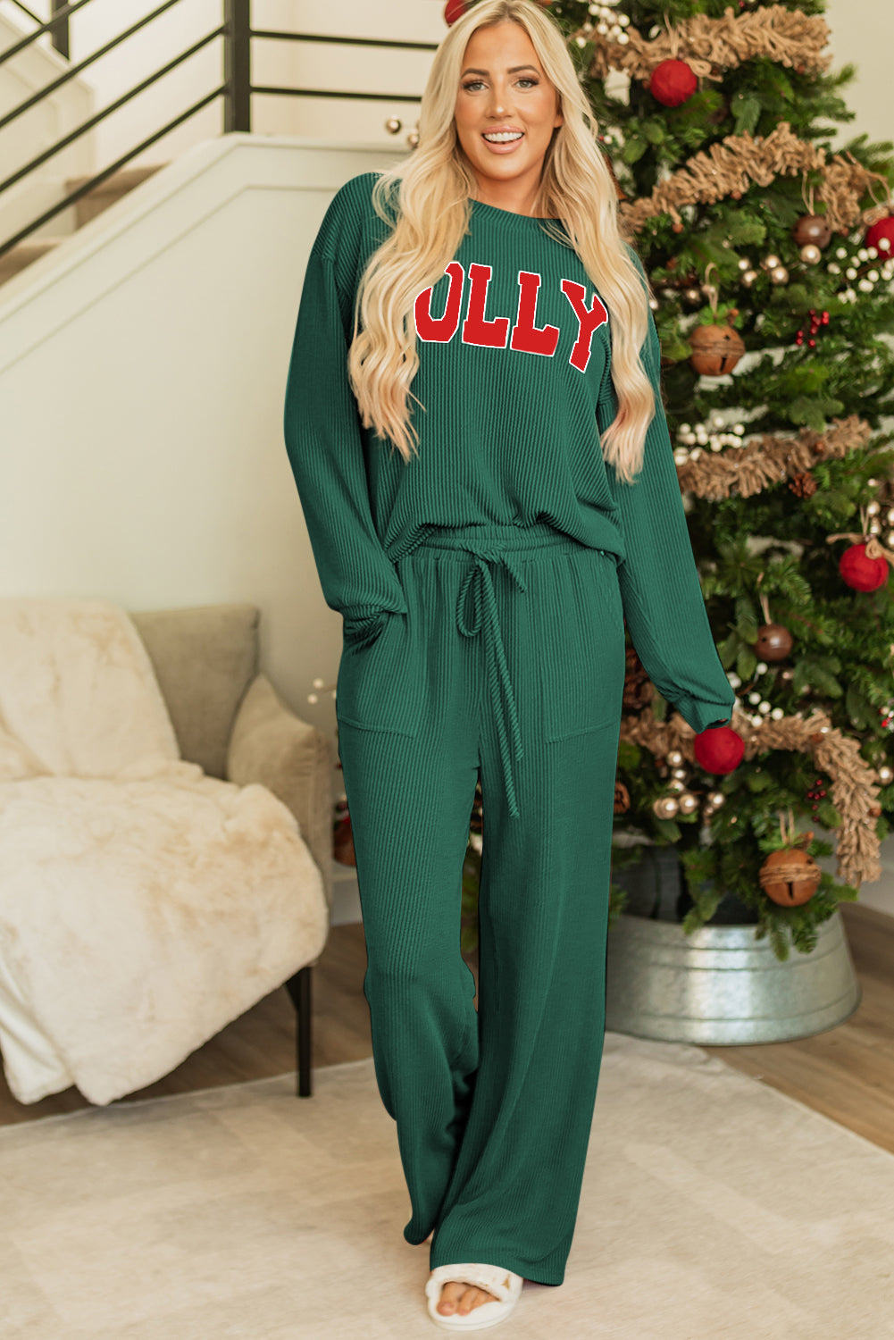 Woman wearing a green outfit with 'Molly' text in red, standing in a room with a Christmas tree.