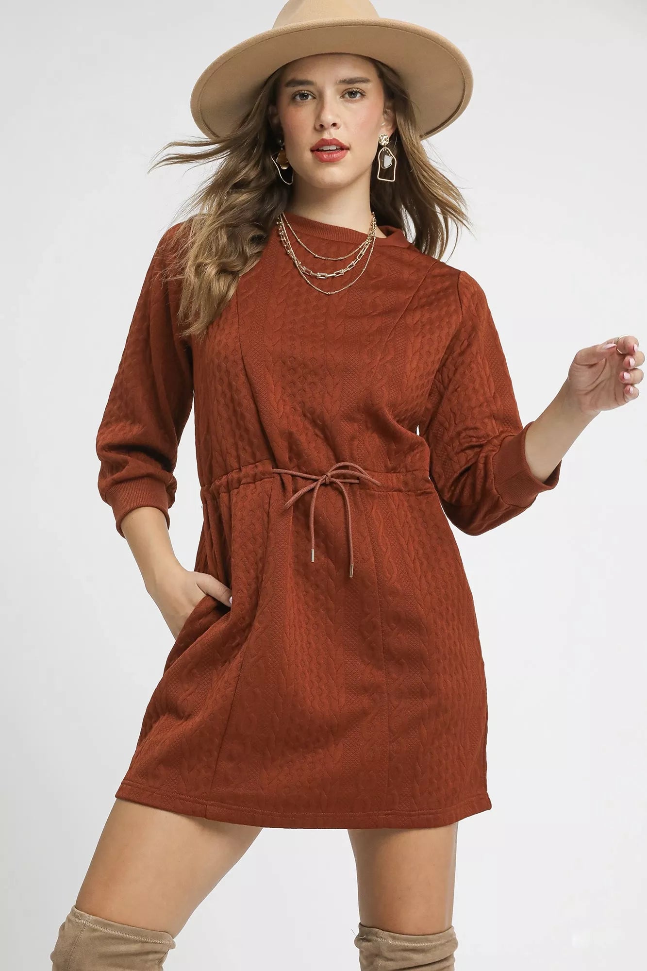 Woman wearing a rust-colored dress with long sleeves and a hat on a white background